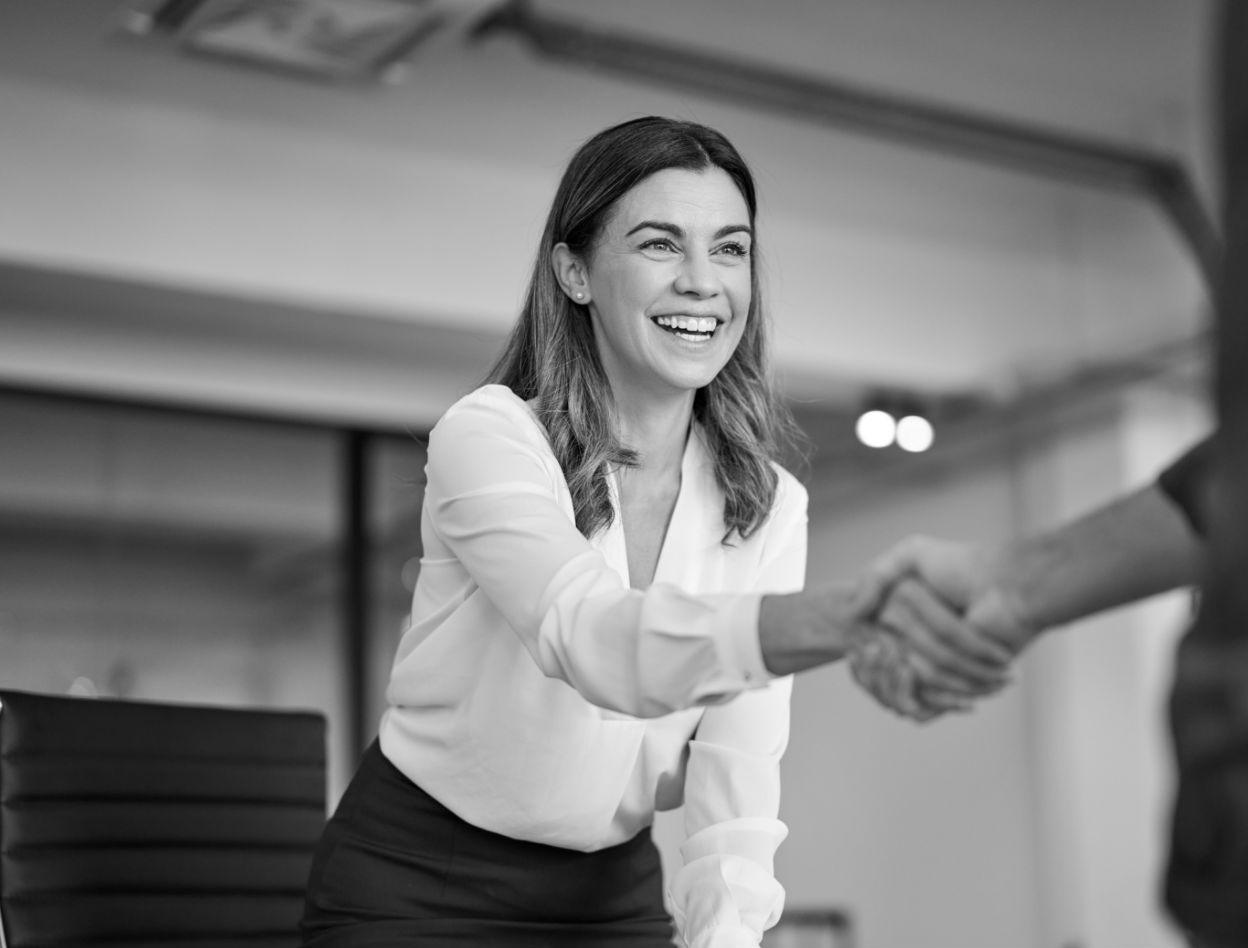 A woman smiling in business attire and shaking hands with another person
