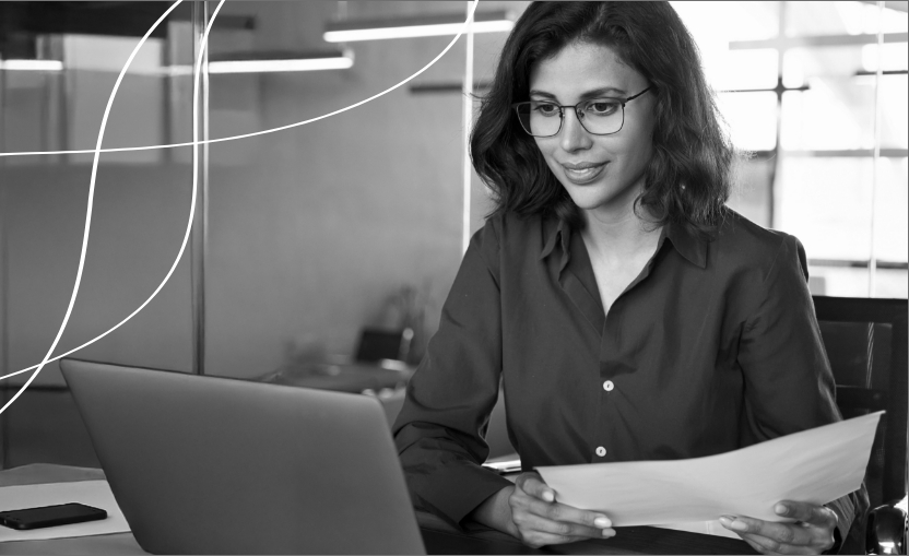 Professional woman reviewing documents while working on a laptop in a modern office setting